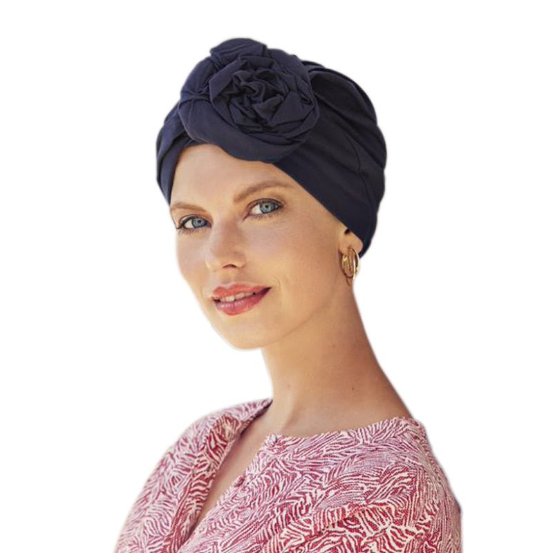 Kvinna med en mörkblå Zuri turban i mjuk bomull med elegant blomdetalj på sidan, leende mot kameran