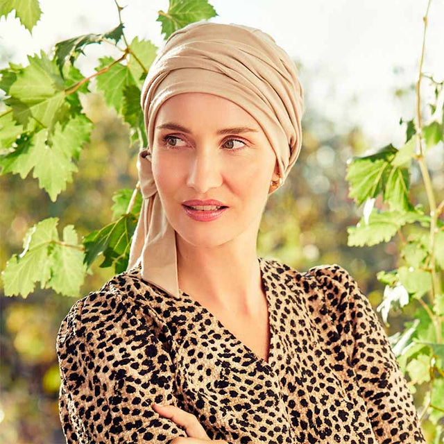 Kvinna med beige B.B. Beatrice turban och leopardmönstrad topp, utomhus bland gröna blad