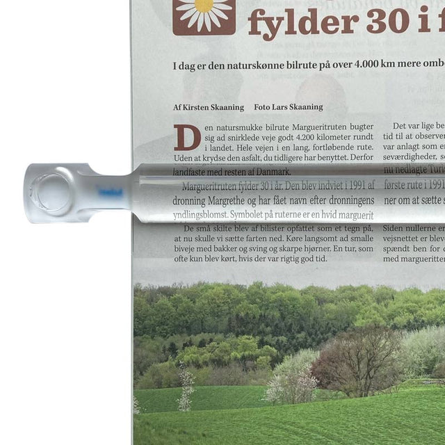 Läslinjal med 2x förstoring placerad över en tidning, visar förstorad text och handtaget