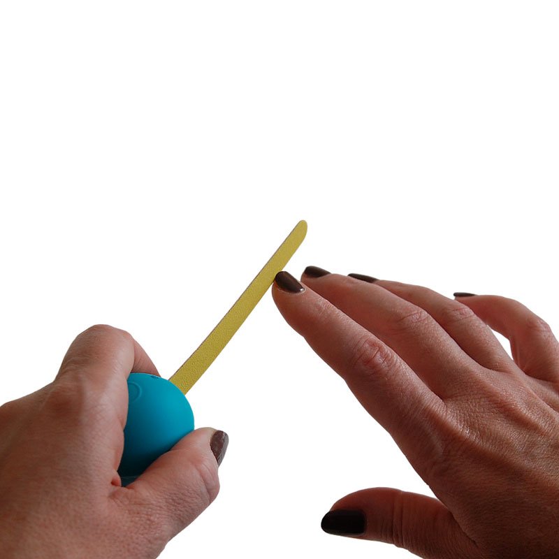 En hand håller en blå GripoBall greppförstoring med en gul nagelfil, redo att fila naglarna