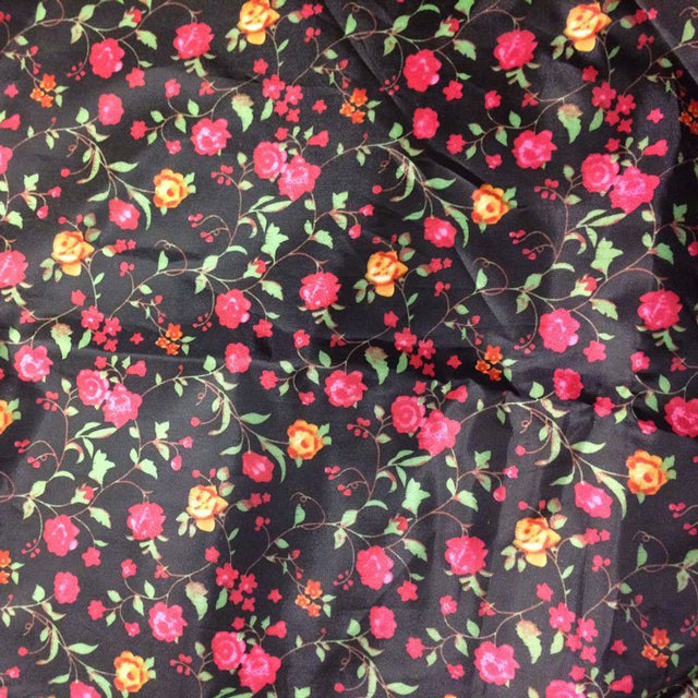 Närbild på haklappens blommiga mönster med små rosa och orange blommor på svart tyg