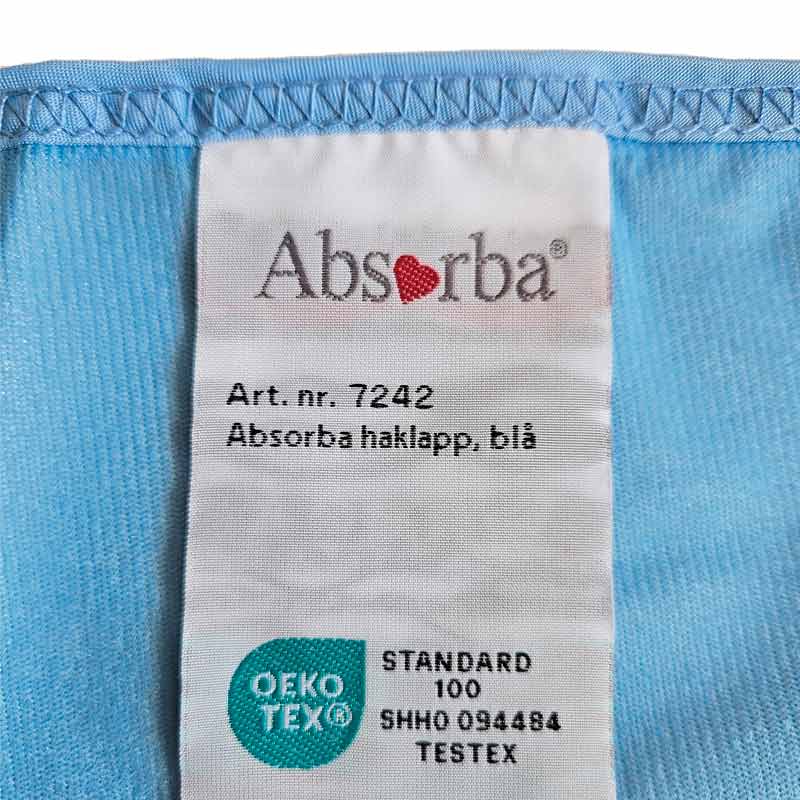 Närbild på tvättlappen på den blå haklappen, visar Absorba-logotypen och Oeko-Tex märkningen