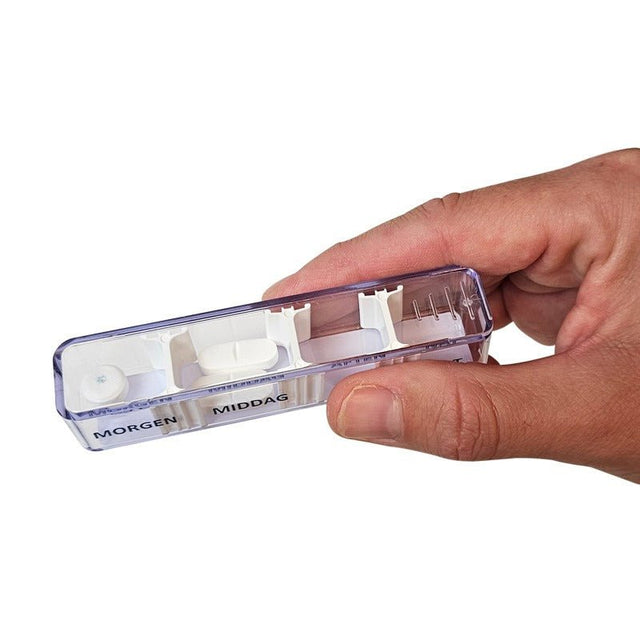 En hand håller en transparent pillerdosa från Dosett veckoset med fyra fack och piller, märkt "Morgen" och "Middag