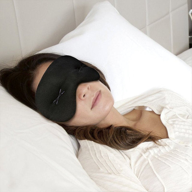 Kvinde sover i seng med sort IMAK sovemaske på, der dækker øjnene og panden