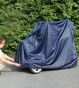 En person sätter på det mörkblå regnskyddet på en permobil, justerar det runt fordonets nedre del