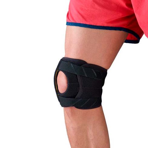 Svart knäskydd med öppen knäskål som bärs på ett ben med röda shorts, sett snett framifrån