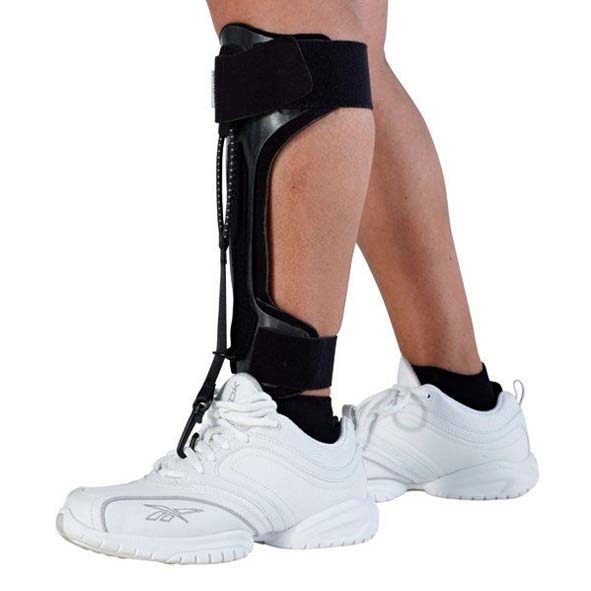 NAVIGAIT™ droppfotsortos i svart plast och tyg, fäst vid en vit sko på en persons ben