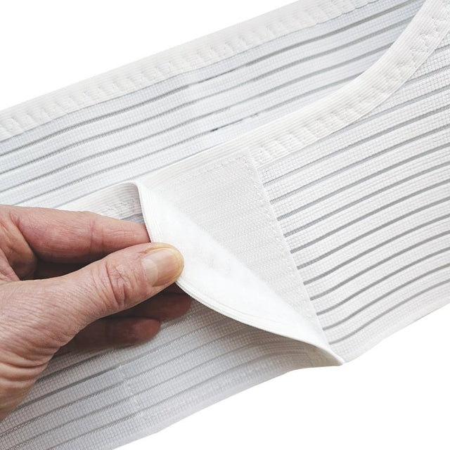 Närbild på en hand som öppnar kardborrebandet på den vita elastiska gördeln med ränder