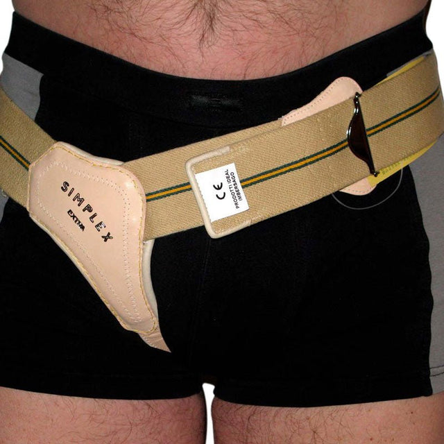 Bråckband i beige med läderkudde, buret av en man över svarta kalsonger för ljumskbråckstöd