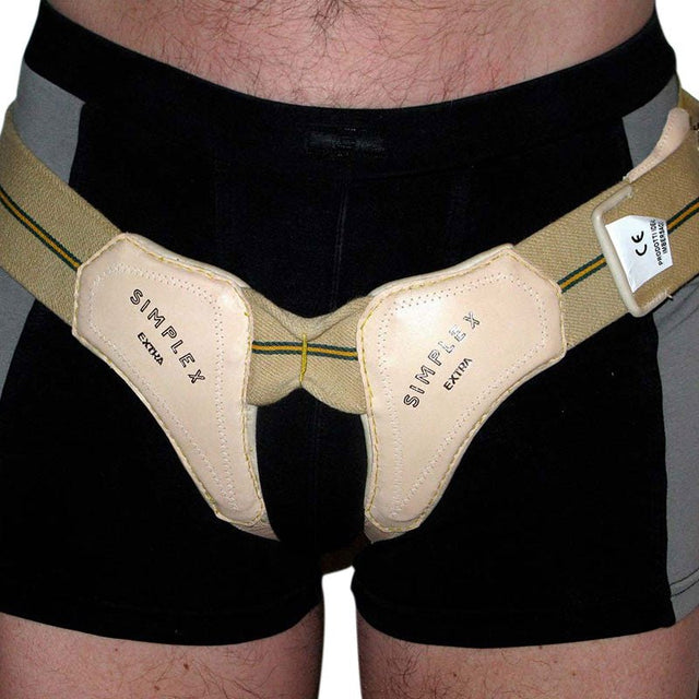 Man som bär ett dubbelsidigt bråckband i beige med två ljusa kuddar över ljumskarna
