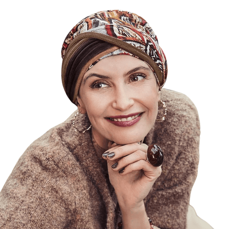 Kvinna bär en Shakti turban i mönstret Tribal Feather med varma höstfärger och fjädrar, leende och tittar åt sidan