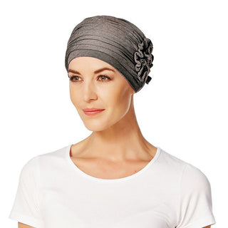 En kvinna visar en mjuk brun Lotus turban med veckad design och en dekorativ blomma