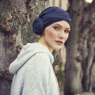Kvinna utomhus med en mörkblå Zuri turban i mjuk bomull med blomdetalj, tittar över axeln